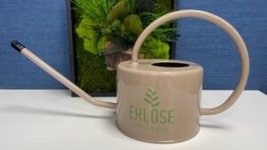 A watering can with a plant in the background.